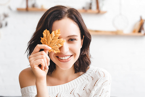 beautiful cheerful girl holding yellow autumn leaf in front of face