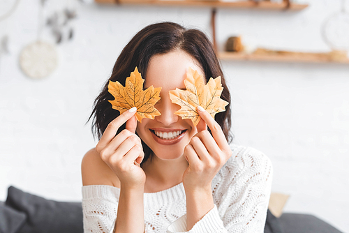 smiling girl holding yellow autumn leaves in front of eyes