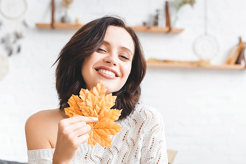 beautiful cheerful woman holding yellow autumn leaves