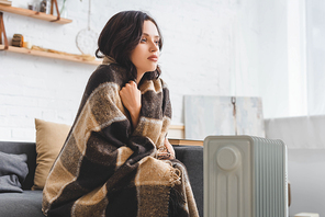 attractive girl warming up with blanket and heater in cold room