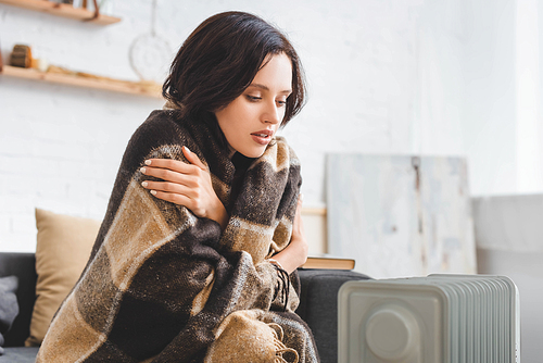 beautiful girl with blanket warming up with heater in cold room