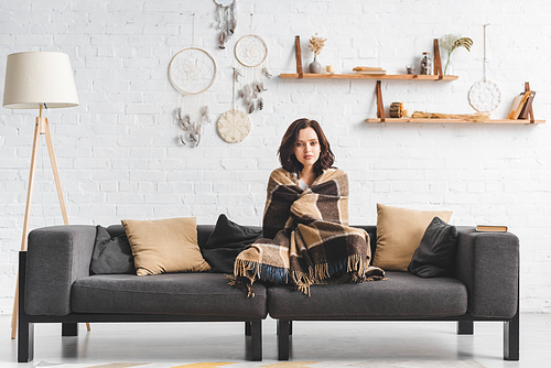 attractive cold girl warming up with blanket on sofa in living room with dream catchers