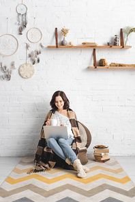 happy woman with cookies and coffee using laptop in living room with dream catchers