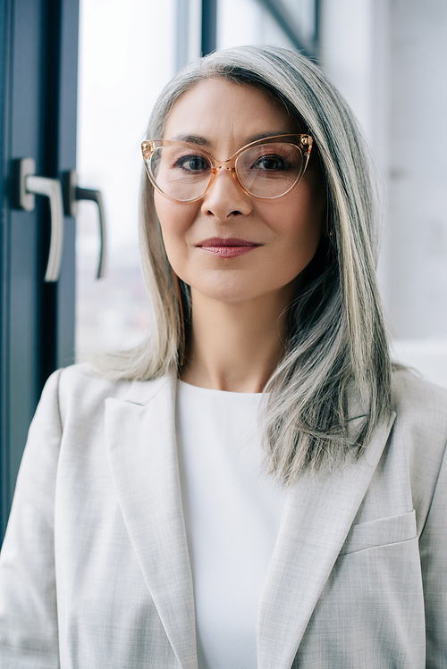 attractive asian businesswoman with grey hair in grey suit and eyeglasses in office