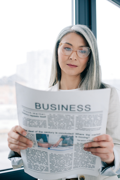 confident asian businesswoman reading business newspaper in office