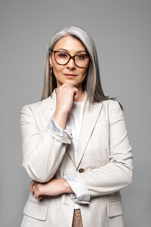 pensive asian businesswoman in eyeglasses isolated on grey