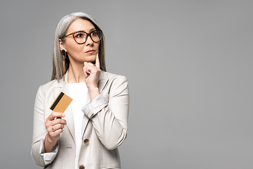 beautiful thoughtful asian businesswoman with grey hair holding credit card isolated on grey