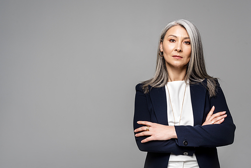confident asian businesswoman with grey hair and crossed arms isolated on grey
