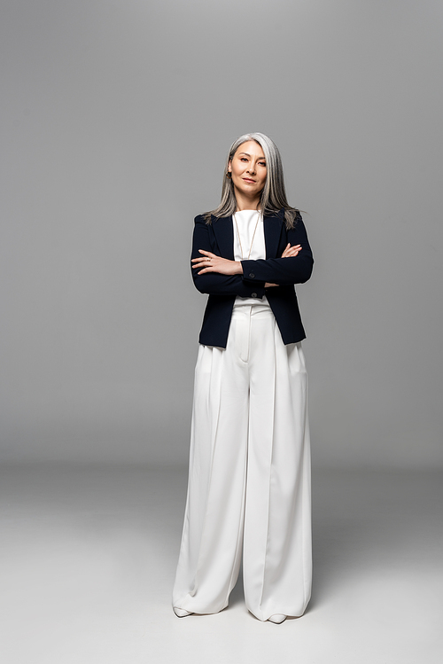 confident asian businesswoman with grey hair and crossed arms on grey