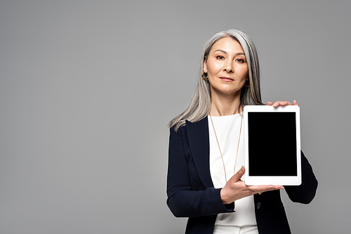 attractive asian businesswoman presenting digital tablet with blank screen isolated on grey