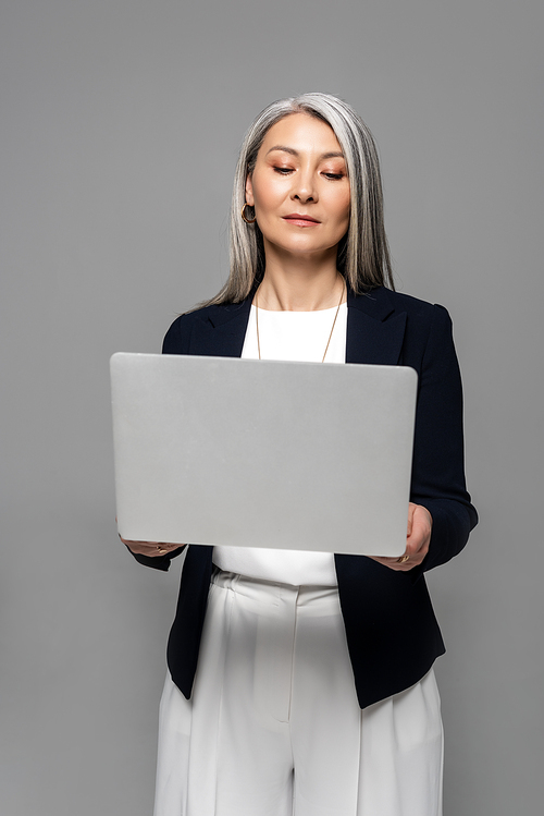 attractive asian businesswoman with grey hair using laptop isolated on grey