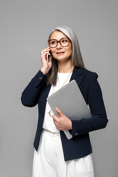 유토이미지 | attractive asian businesswoman with grey hair talking on smartphone and holding laptop isolated on grey