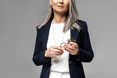 cropped view of businesswoman with grey hair holding eyeglasses isolated on grey