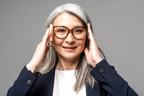 smiling asian businesswoman with grey hair in eyeglasses isolated on grey
