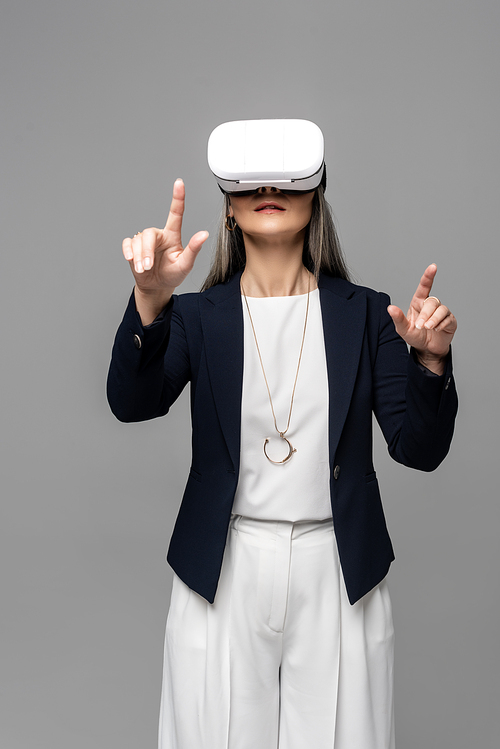 corporate businesswoman pointing and using virtual reality headset isolated on grey