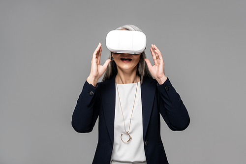 attractive surprised businesswoman using virtual reality headset isolated on grey