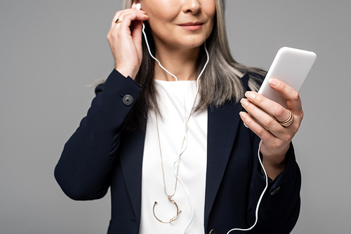 cropped view of businesswoman with grey hair listening music with earphones and smartphone isolated on grey