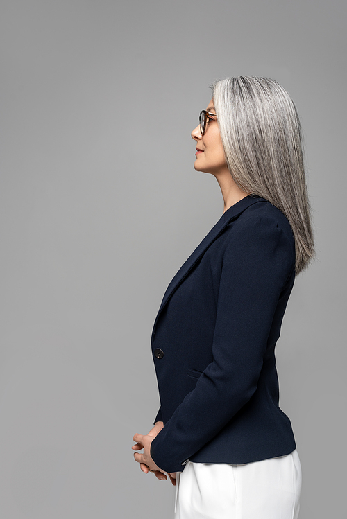 side view of asian businesswoman with grey hair in eyeglasses isolated on grey