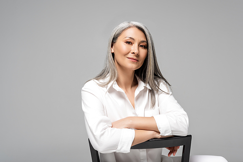 attractive asian woman with grey hair sitting on chair isolated on grey