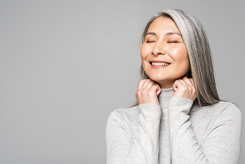 happy asian woman in turtleneck with grey hair and closed eyes isolated on grey
