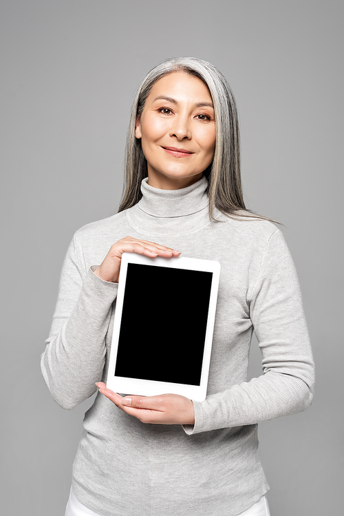 happy attractive asian woman presenting digital tablet with blank screen isolated on grey