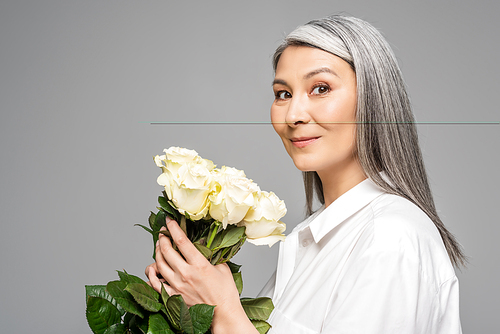 adult smiling asian woman with grey hair holding bouquet of white roses isolated on grey