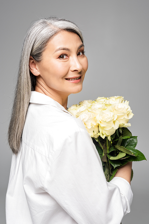 adult asian woman with grey hair holding bouquet of white roses isolated on grey