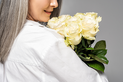 cropped view of adult woman with grey hair holding bouquet of white roses isolated on grey
