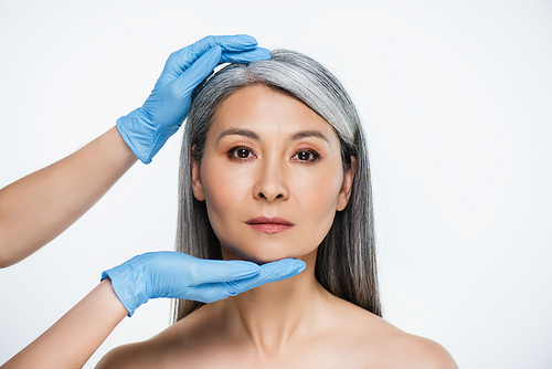 doctor in latex gloves touching face of attractive naked asian woman isolated on grey