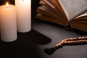 holy bible with rosary on black dark background with burning candles