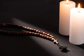 rosary on black dark background with burning candles