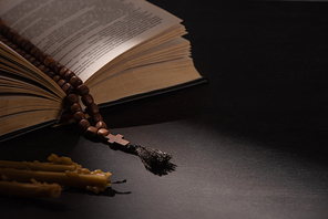 holy bible with rosary on black dark background with candles