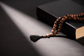 holy bible with rosary on black dark background with sunlight