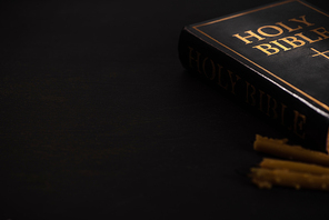 selective focus of holy bible and candles on black dark background