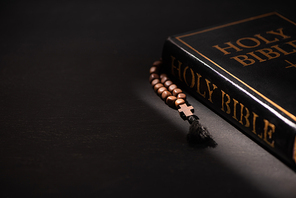 holy bible with rosary on black dark background with burning candles