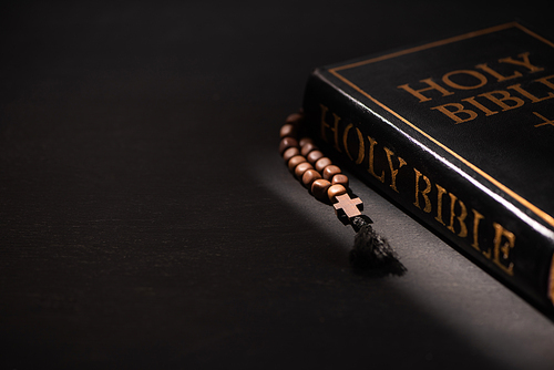 holy bible with rosary on black dark background with burning candles
