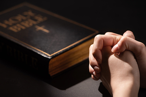 cropped view of woman praying near holy bible in dark
