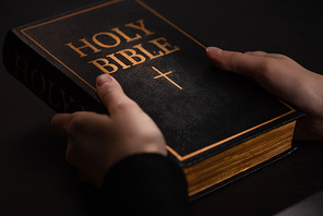cropped view of woman holding holy bible in dark