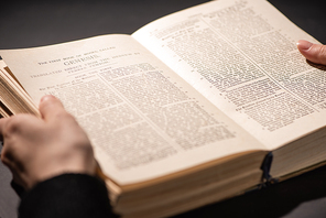 cropped view of woman reading holy bible in dark with sunlight