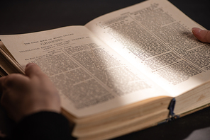 cropped view of woman holding holy bible in dark with sunlight