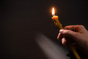 cropped view of woman holding burning church candle in dark