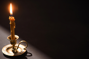 church candle in candlestick burning in dark with sunlight