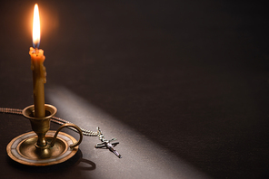 church candle in candlestick burning near catholic cross in dark with sunlight