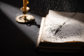 selective focus of candlestick near bible with catholic cross and ashes in dark with sunlight