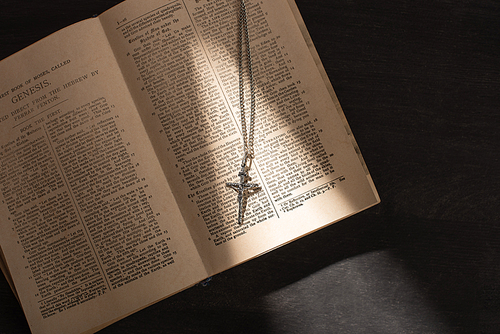 top view of open holy bible with cross on dark background with sunlight