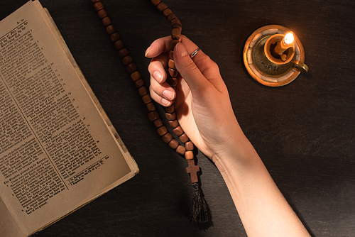 cropped view of woman praying with rosary near open holy bible and candle