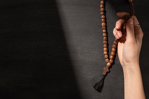 cropped view of woman praying with rosary on dark background