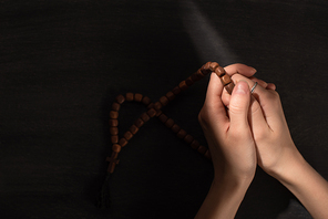 cropped view of woman praying with rosary on dark background