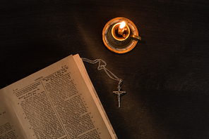 top view of open holy bible with cross and candle on dark background