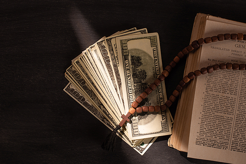 top view of holy bible with money and rosary on dark background with sunlight